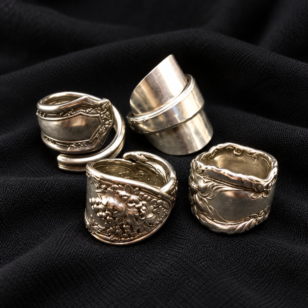 A collection of ornate silver spoon rings displayed on black cloth